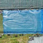 Luftaufnahme eines Fahrsilos, das mit einer OXY MAX 50 Silofolie abgedeckt wird. Neben dem Silo sind Schutzgitter und Sandsäcke zur Beschwerung zu sehen.
