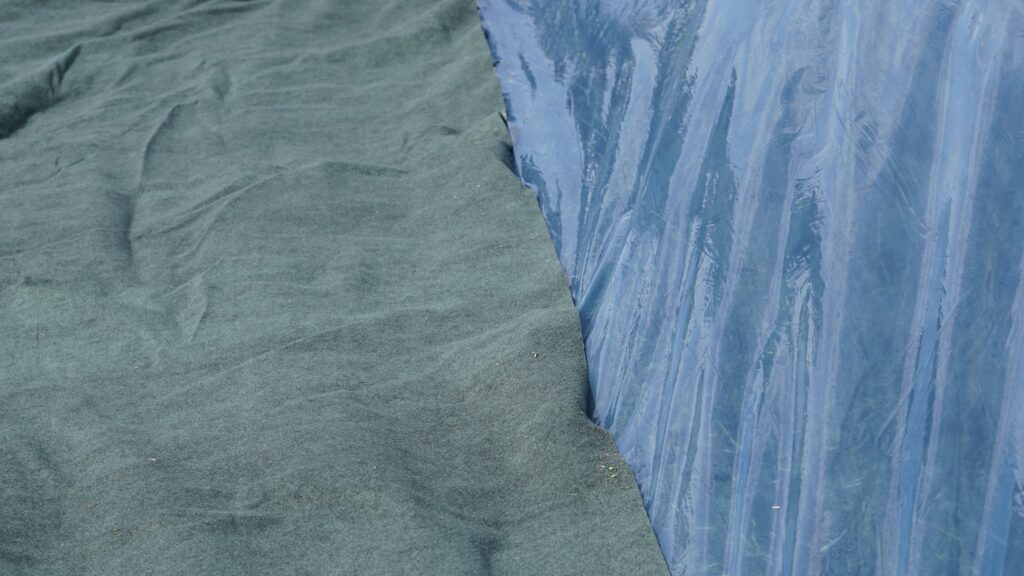 Die blaue Silofolie OXY MAX 50 auf einem Gras-Silage, die zur Hälfte mit dem OXY Protec Vlies zum Schutz abgedeckt ist.